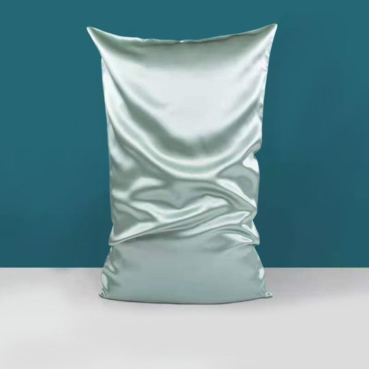 The SusanSilk 22 Momme High Gloss Silk Pillowcase Envelope, in a large size and light blue color, stands upright against a teal wall and grey floor backdrop, displaying slight wrinkles on its silky fabric.