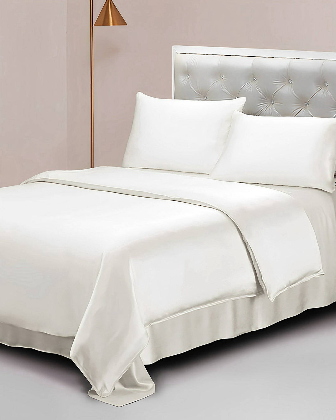 A neatly made bed adorned with a SusanSilk 25 Momme Seamless Luxury Duvet Cover, two pillows, and a tufted headboard stands next to a tall brass floor lamp, exuding the elegance of SusanSilk.