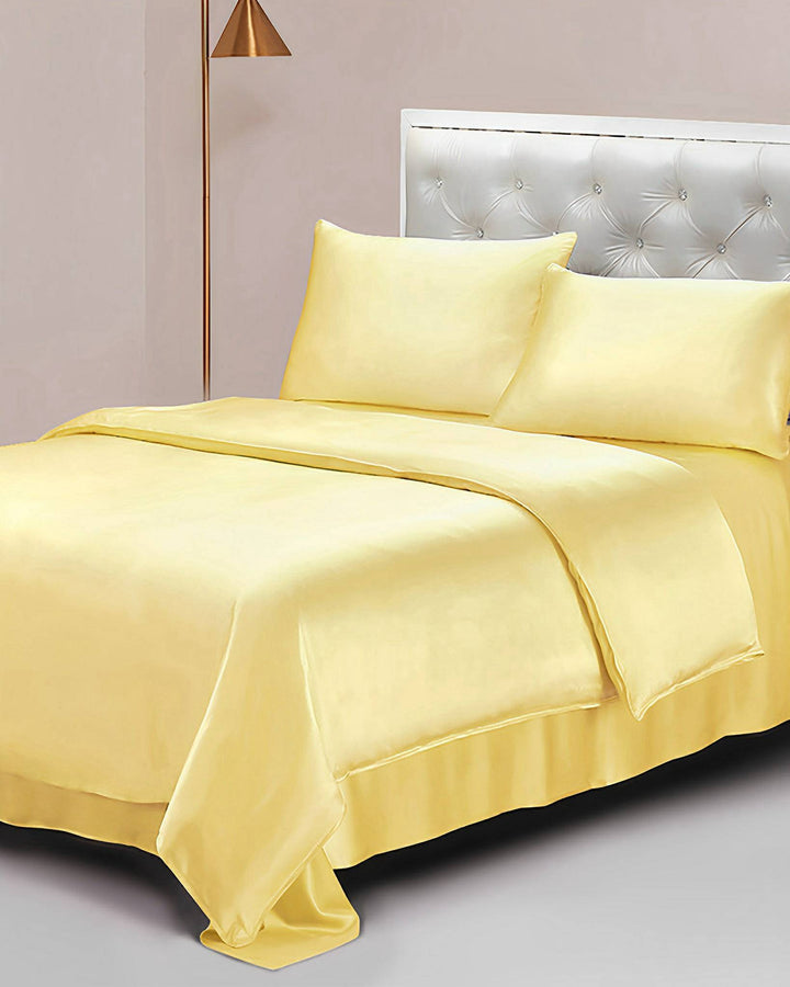 A neatly made bed featuring SusanSilk's 25 Momme Seamless Luxury Duvet Cover in a vibrant yellow, two pillows, and a white tufted headboard. A brass floor lamp stands beside the bed.