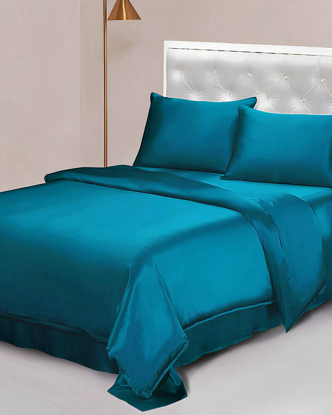A neatly made bed with teal 25 Momme Seamless Luxury Duvet Cover, pillows, and sheet. The bed has a white tufted headboard and features opulent SusanSilk accents. A tall gold-colored floor lamp stands beside it.