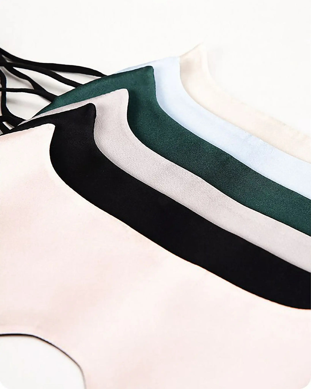 A row of SusanSilk's Cat Shape Silk Eye Masks in various colors, including white, black, green, and beige, is laid out flat on a light surface.