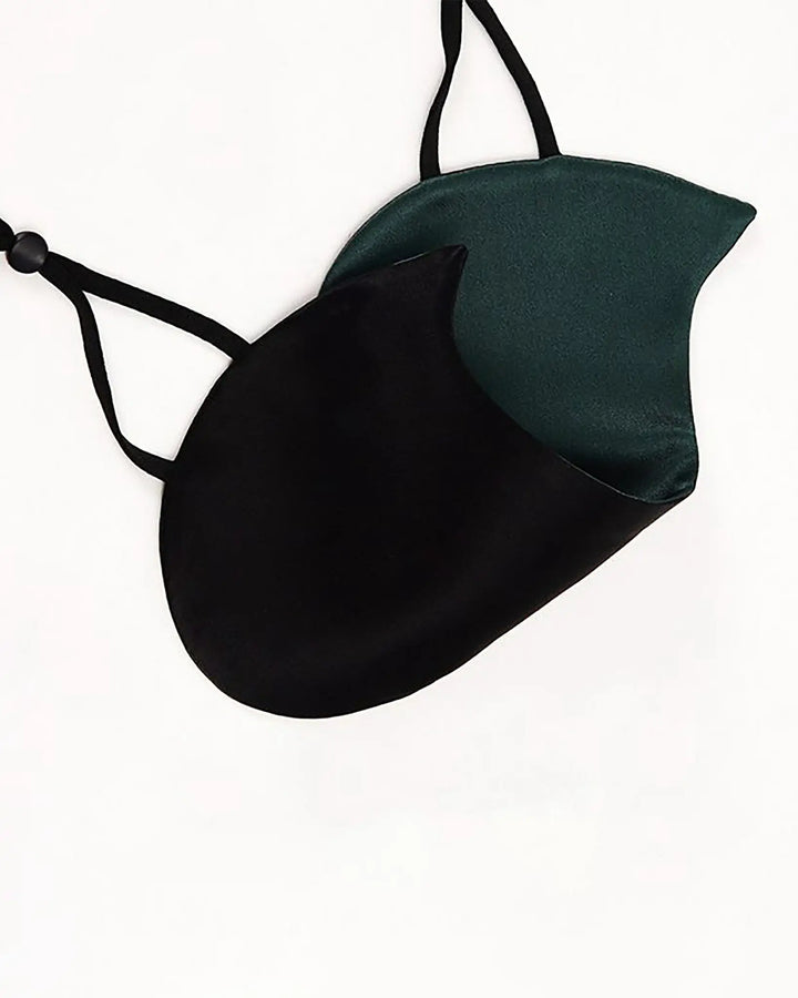 A black and green Cat Shape Silk Eye Mask from SusanSilk with adjustable straps lies on a white surface.