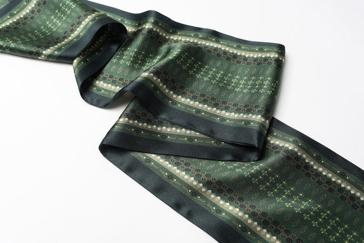 The Dark Green Daisy Silk Long Fluttering Belt by SusanSilk, featuring luxurious green and black silk with a striped and geometric pattern, is laid out on a flat, white surface.