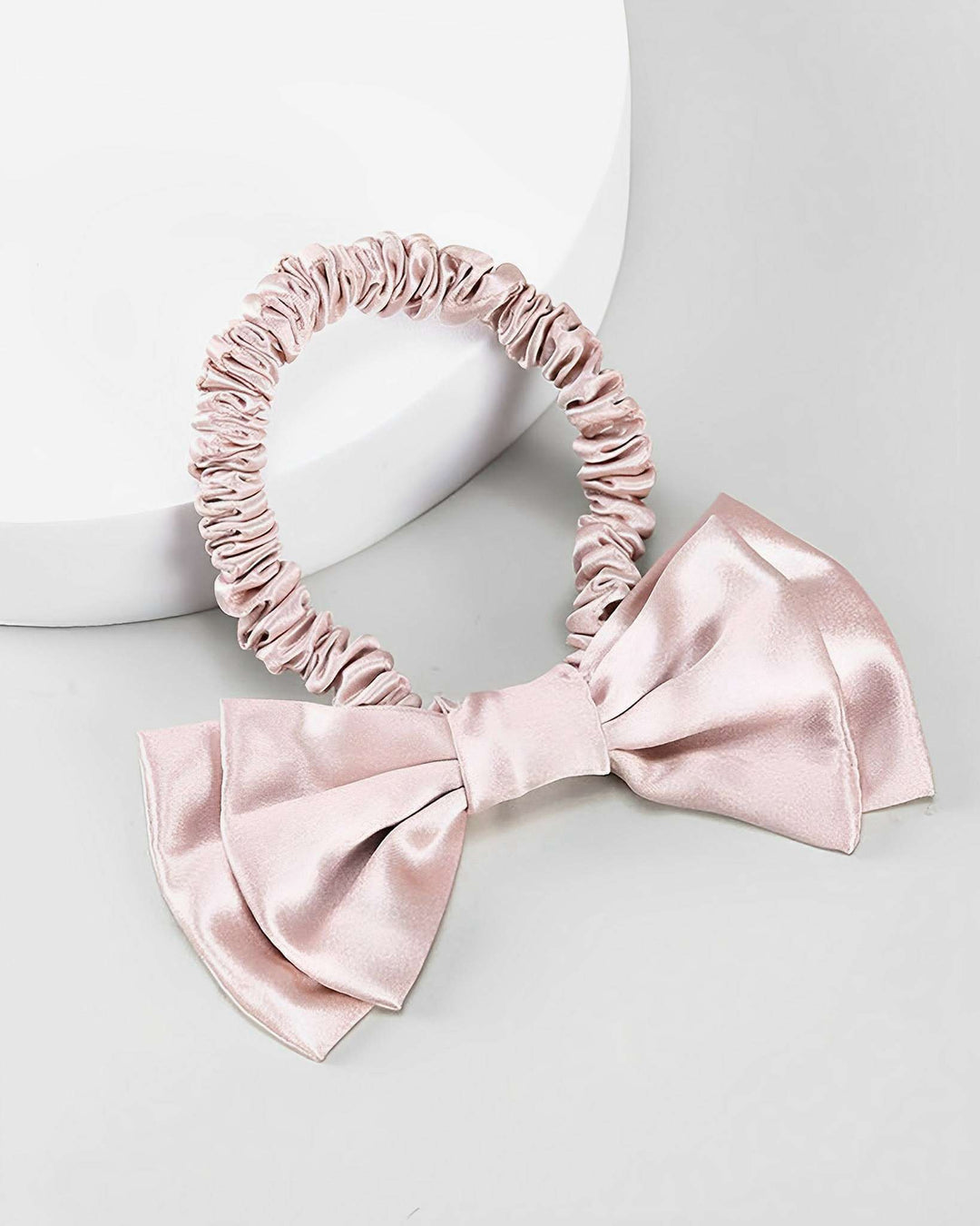 A light pink Vintage Bow-Knot Silk Scrunchie by SusanSilk, featuring an attached large bow, placed on a white and gray background.