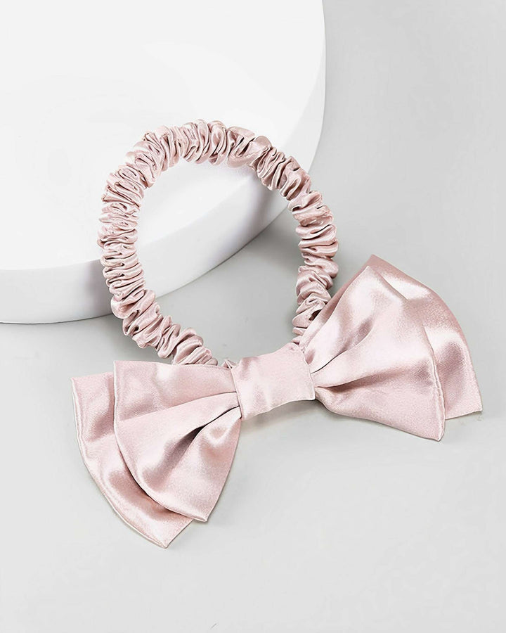 A light pink Vintage Bow-Knot Silk Scrunchie by SusanSilk, featuring an attached large bow, placed on a white and gray background.