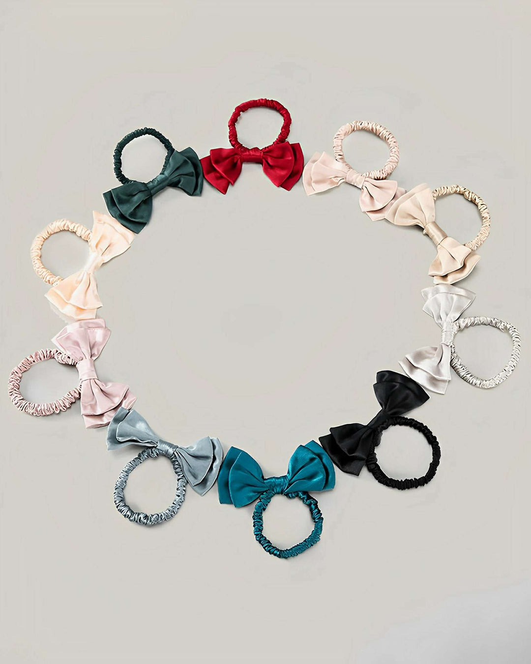 A circle of SusanSilk Vintage Bow-Knot Silk Scrunchies in various colors, including red, black, teal, light blue, pink, and cream, arranged on a light grey background.
