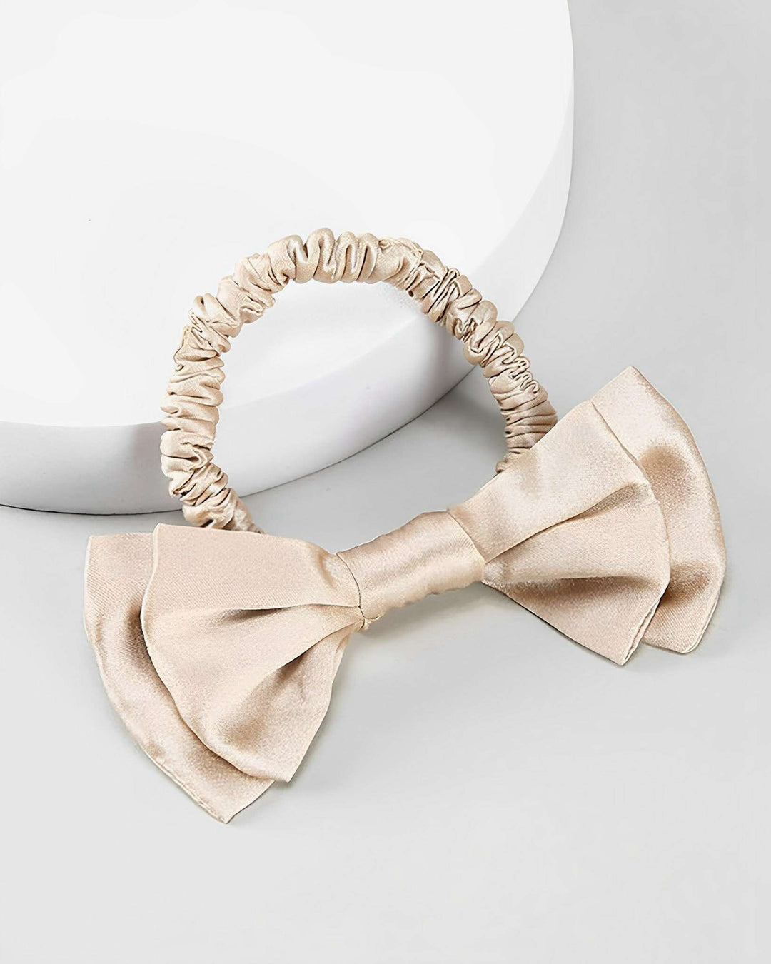 A Vintage Bow-Knot Silk Scrunchie from SusanSilk in elegant beige satin, featuring a large decorative bow, displayed on a white surface.