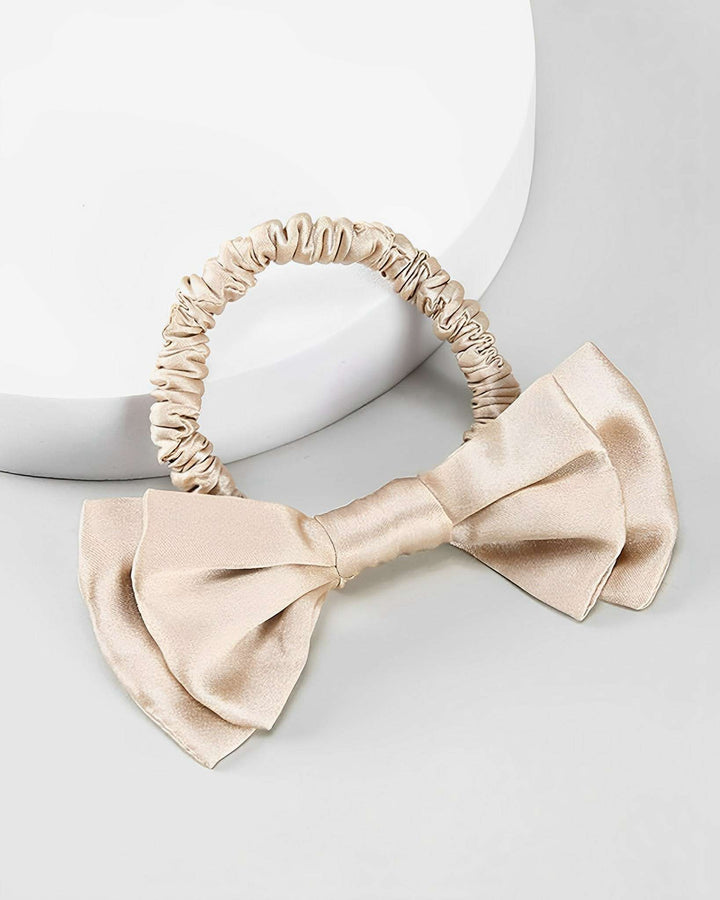 A Vintage Bow-Knot Silk Scrunchie from SusanSilk in elegant beige satin, featuring a large decorative bow, displayed on a white surface.