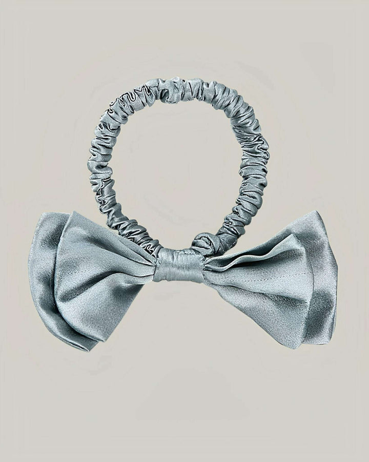 The Vintage Bow-Knot Silk Scrunchie from SusanSilk, featuring a light gray hue and a decorative center bow, is showcased against a plain gray background.