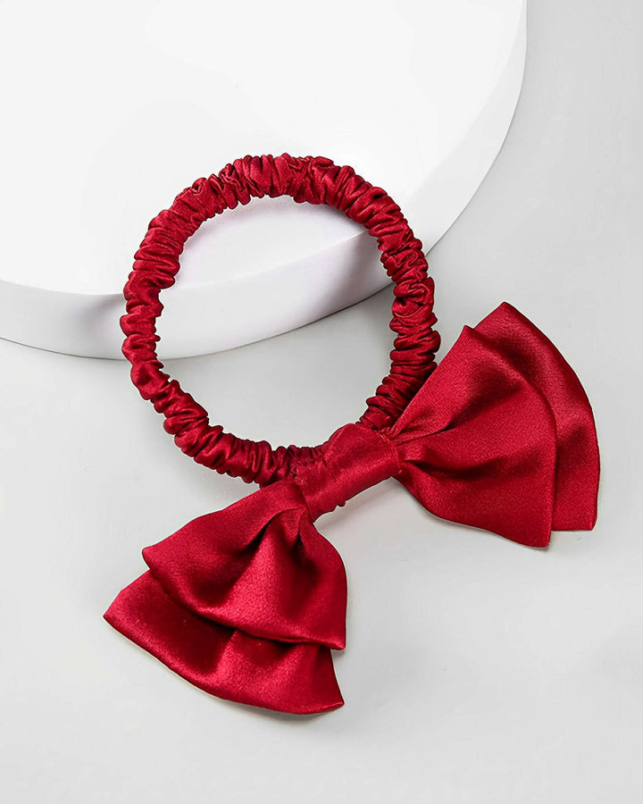 A Vintage Bow-Knot Silk Scrunchie from the SusanSilk brand, featuring a large matching bow and crafted from sleek silk material, is placed on a white circular surface.