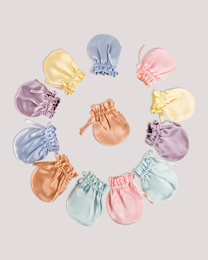Flat lay of 19 Momme mulberry silk baby mittens in six pastel colors, designed to help prevent face scratching while protecting delicate newborn skin.