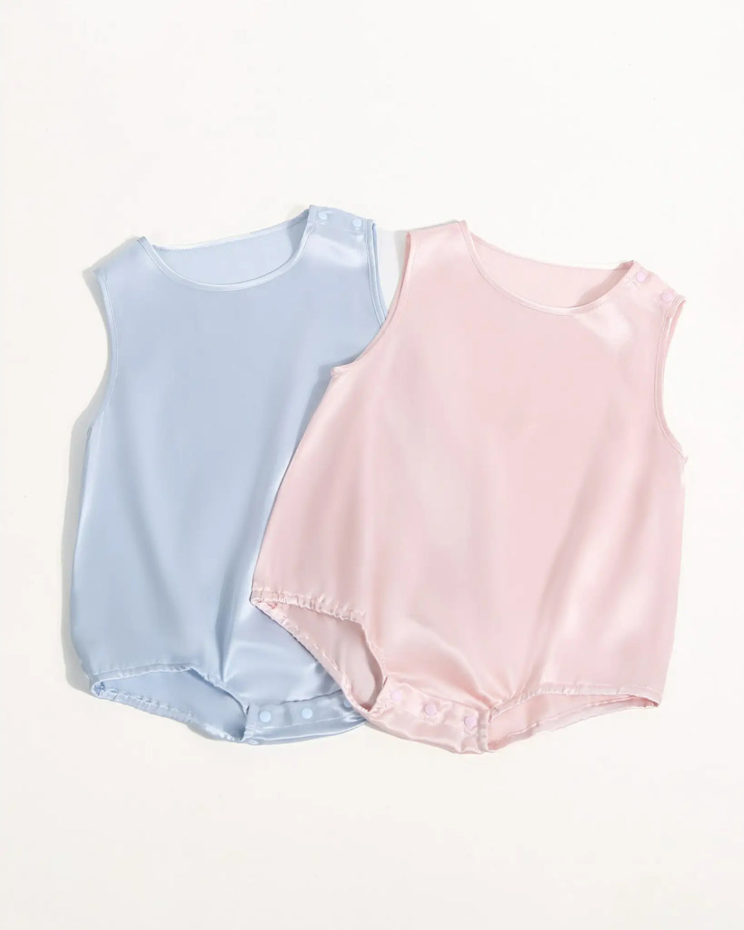 Three 19 Momme Silk Baby Button Onesies from SusanSilk in pastel colors (white, pink, and cream) are arranged side by side on a plain background. Each onesie features snap buttons on the shoulders and elastic leg openings, showcasing the gentle touch of SusanSilk for your baby's comfort1.