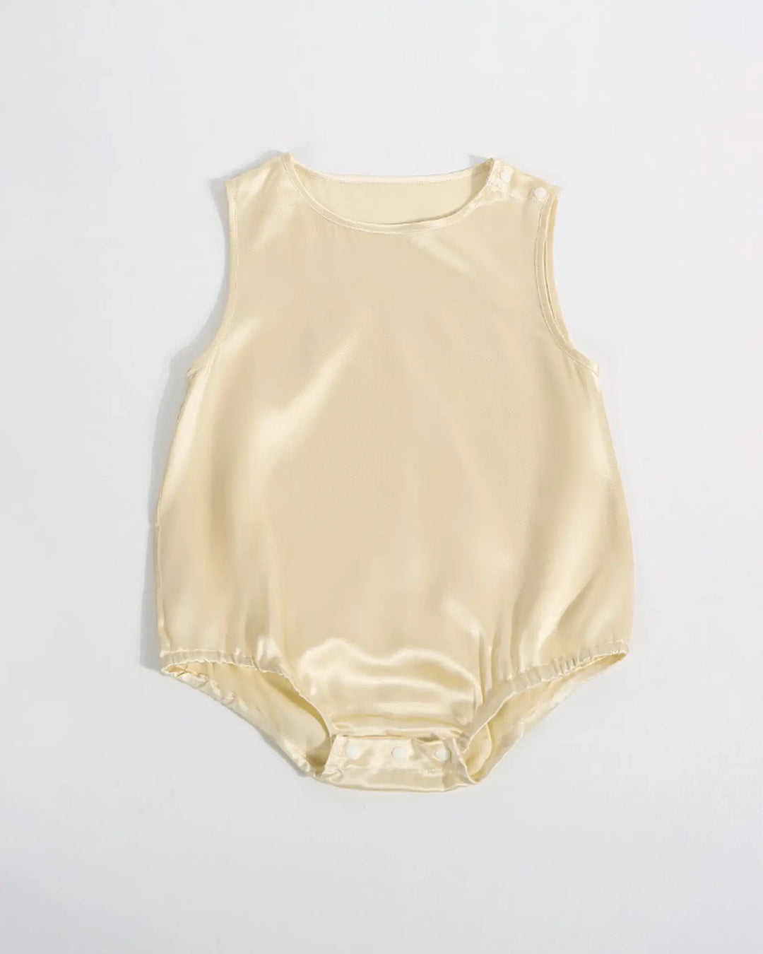 The 19 Momme Silk Baby Button Onesie by SusanSilk is a sleeveless, light beige baby romper made from soft silk, featuring a round neckline, shoulder snap buttons, and bottom snap closures