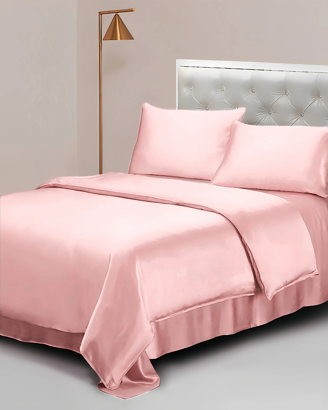 Pink satin bedding set on a bed with a lamp and headboard in the background.