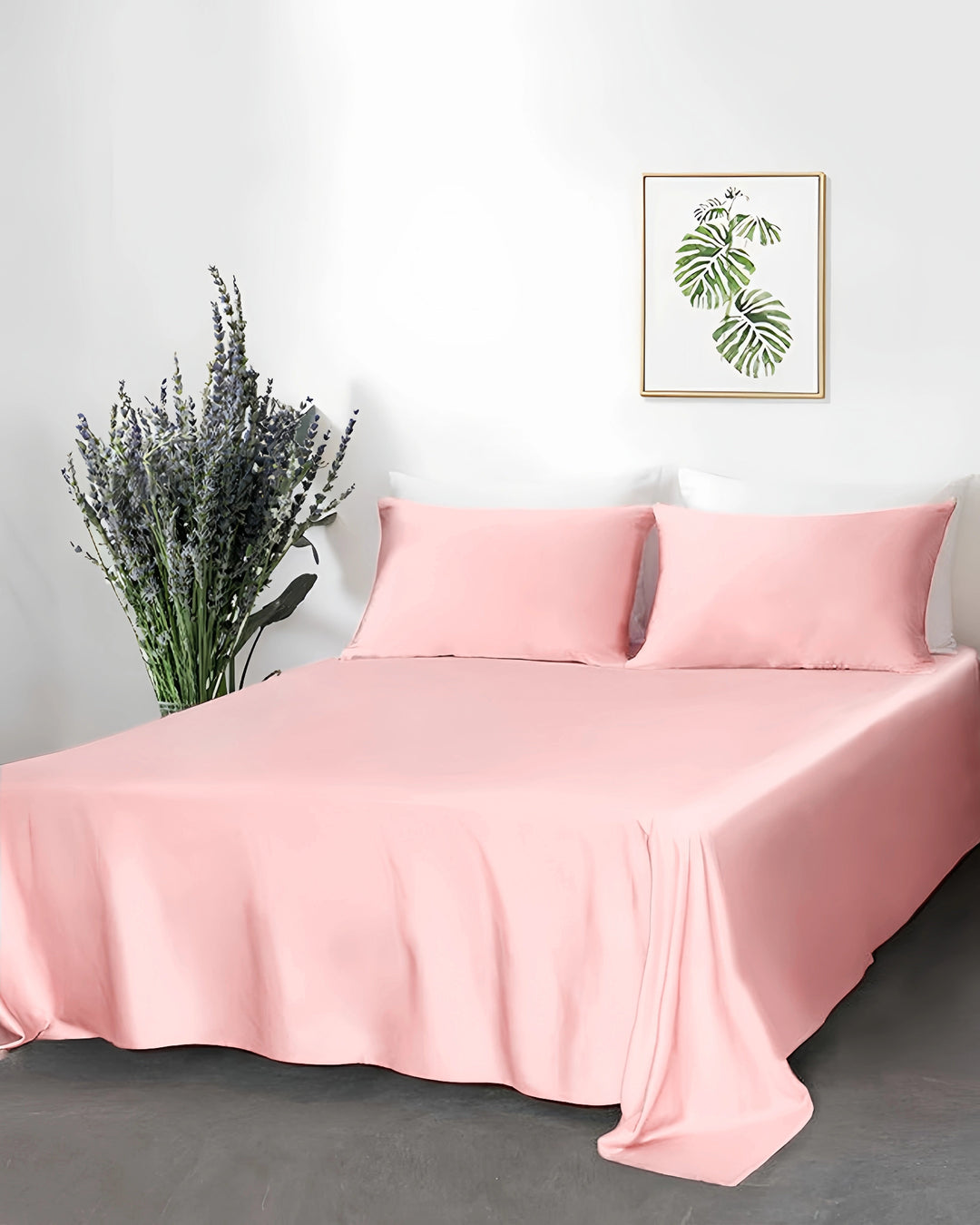Pink satin sheet set on a bed with a decorative plant and wall art in the background.