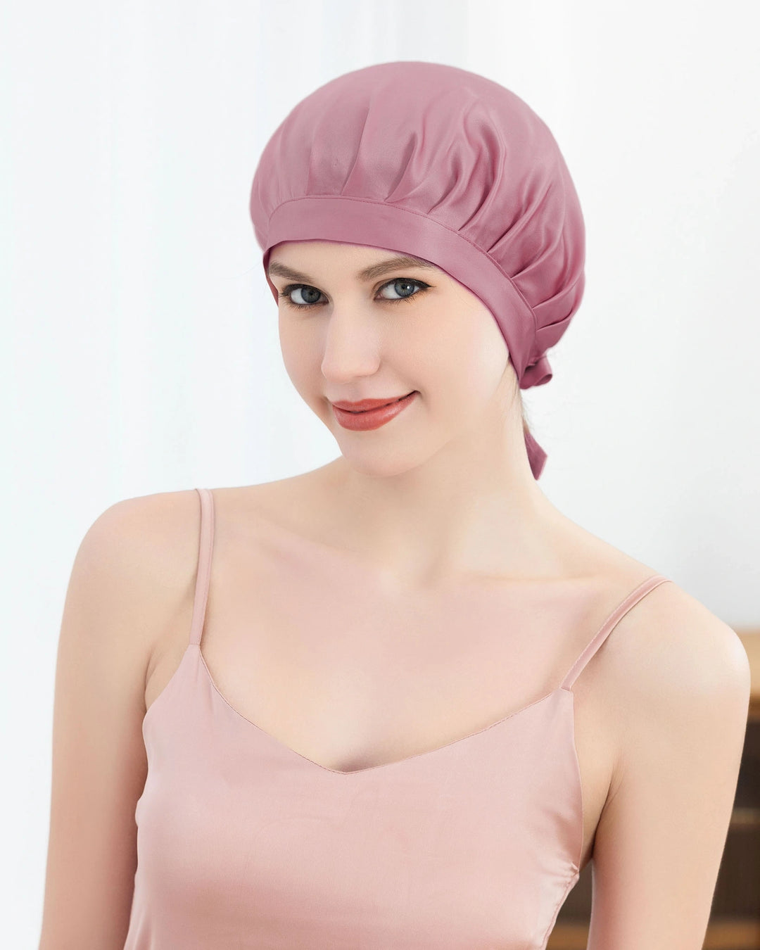 Woman wearing a pink satin bonnet against a white background