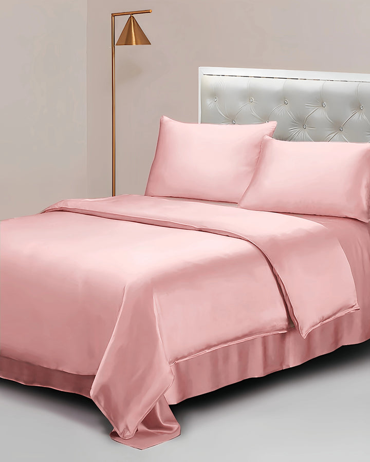 Pink satin bedding set on a bed with a lamp and headboard in the background.