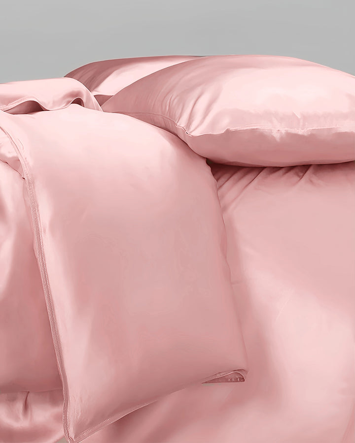 Pink satin bedding set with pillows on a light gray background