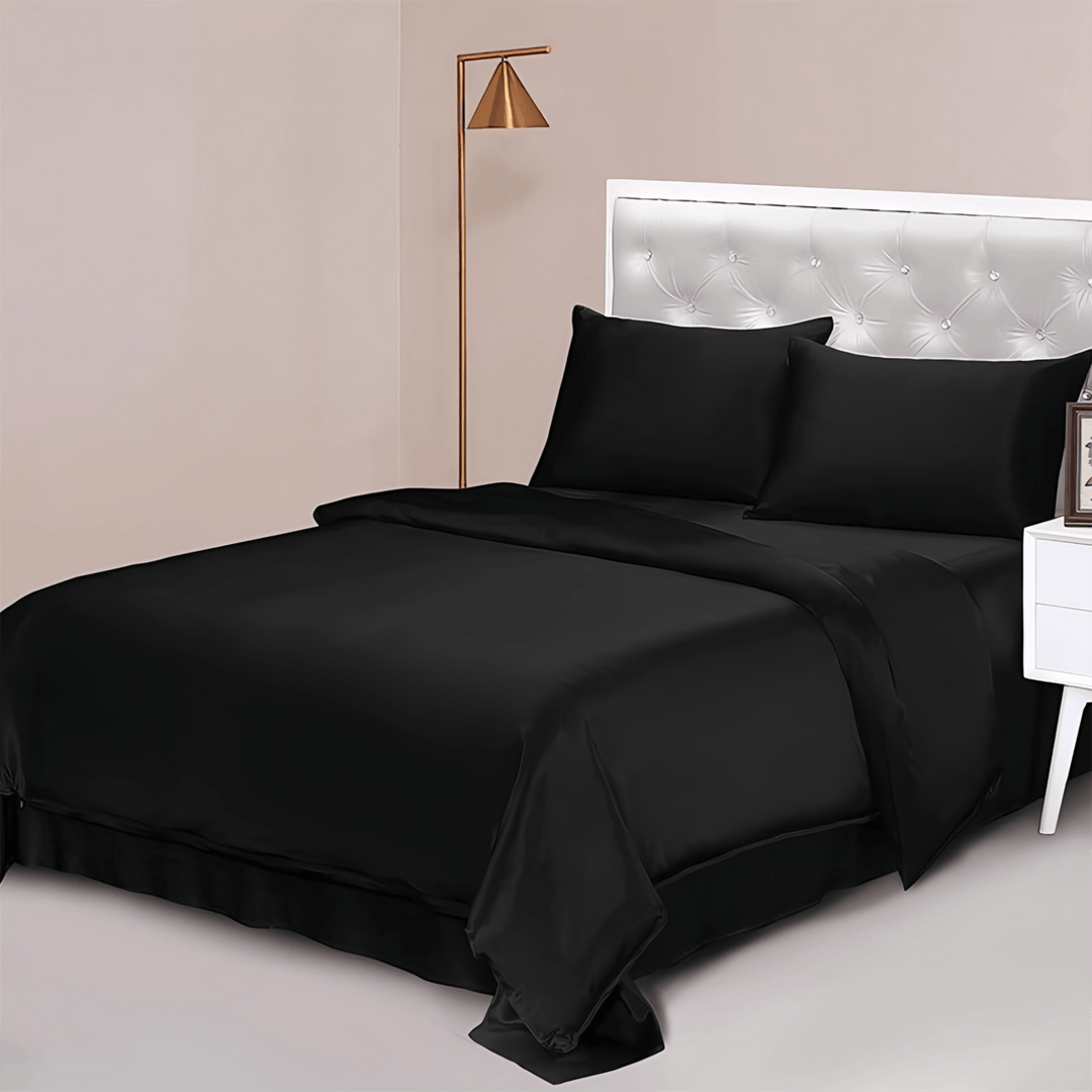 A neatly made bed featuring the 25 Momme Luxury Silk Bedding Set - 4Pcs by SusanSilk in black, two pillows, a white tufted headboard, a side table with a picture frame, and a floor lamp in the corner of the room.