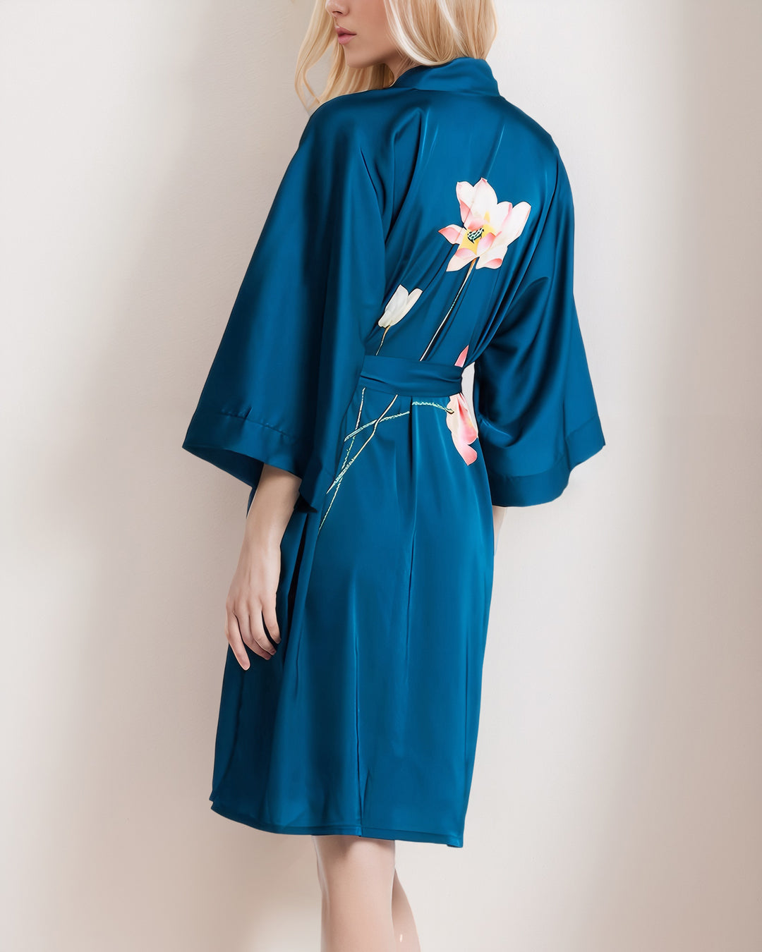 A woman is wearing a Lotus Style Short Silk Kimono by SusanSilk in teal, adorned with floral designs on the back. She is standing and facing away from the camera.