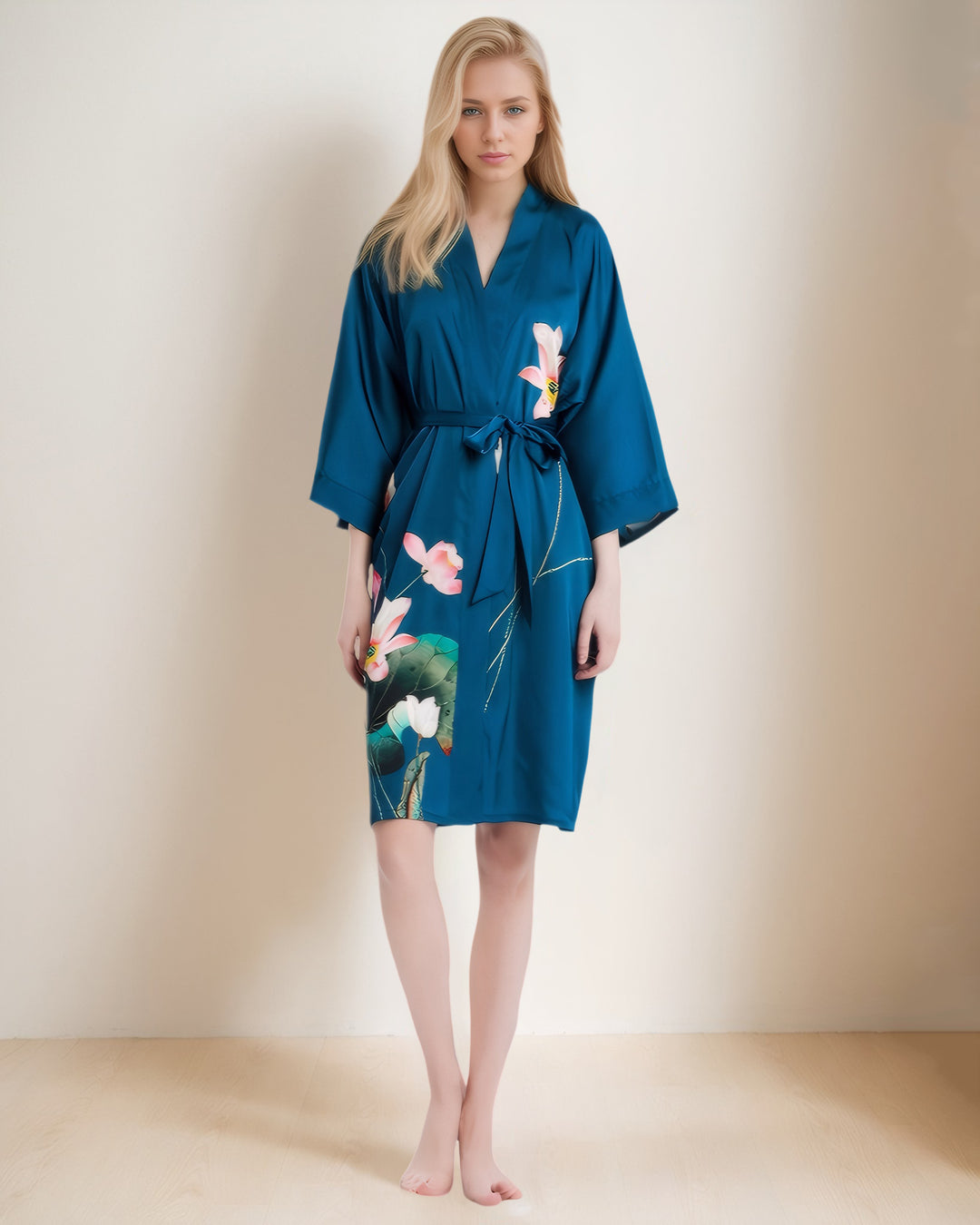 A person with light-colored hair stands against a plain background, wearing the Lotus Style Short Silk Kimono by SusanSilk, featuring luxurious florally designed fabric in blue, tied at the waist.