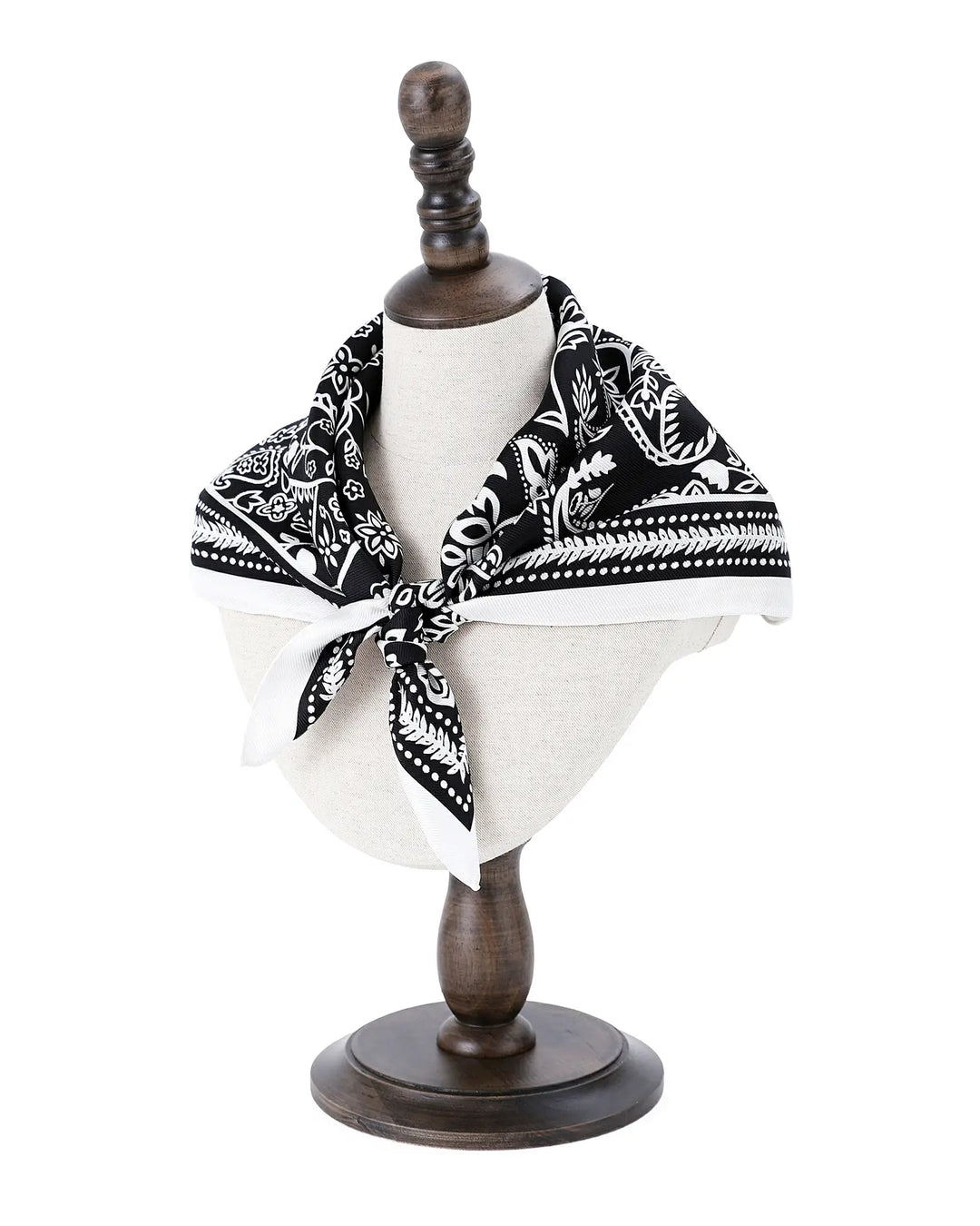 Mannequin head with a black and white patterned scarf on a wooden stand against a white background