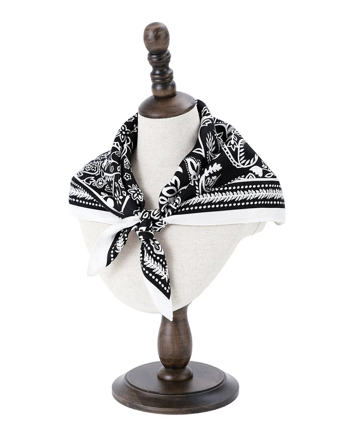 Mannequin head with a black and white patterned scarf on a wooden stand against a white background
