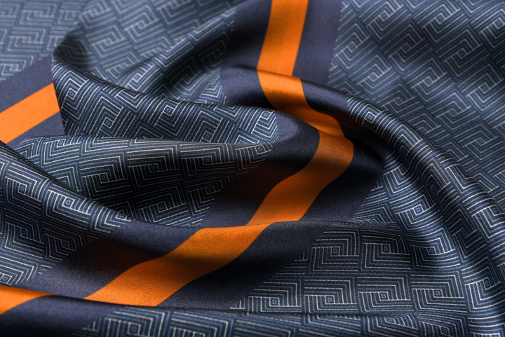A close-up of a SusanSilk Luxurious Men's Silk Twill Scarf in blue and yellow, showcasing an intricate geometric maze-like design.