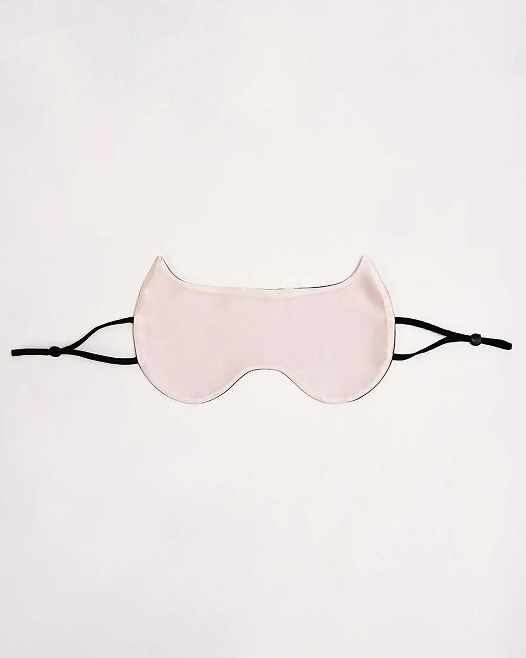 The Cat Shape Silk Eye Mask by SusanSilk, featuring pale pink silk material and black adjustable straps, is laid flat against a white background.
