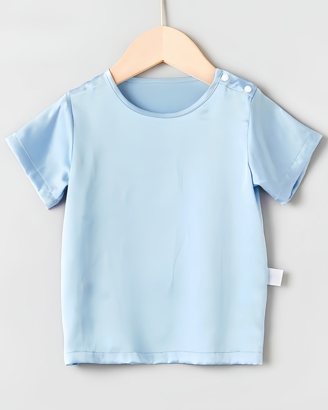 The Sky Blue 19 Momme Baby & Toddler Silk Short Sleeve Top by SusanSilk, featuring a round neckline and side button, hangs on a wooden hanger against a light background—feeling just like baby's second skin.