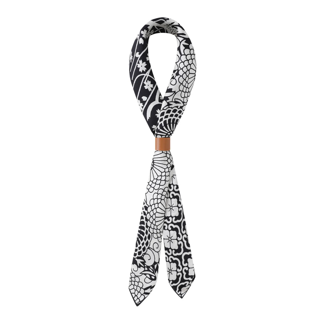 A Seeker Black Square Silk Scarf by SusanSilk, featuring a black and white pattern, tied in a loop with a tan ring around the knot.