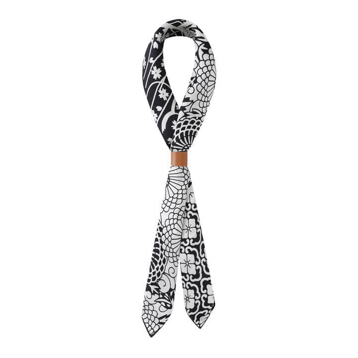 A Seeker Black Square Silk Scarf by SusanSilk, featuring a black and white pattern, tied in a loop with a tan ring around the knot.