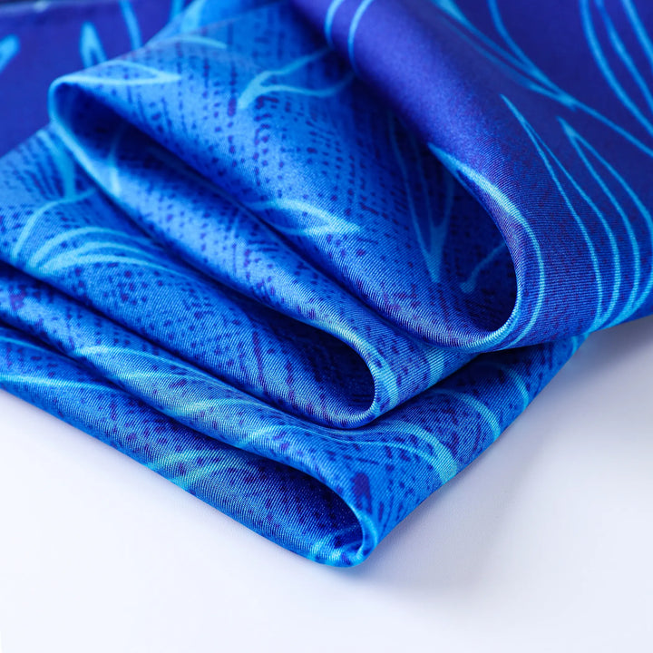 Close-up of folded blue fabric with intricate patterns and light blue accents, reminiscent of the Blue Sky Square Silk Scarf by SusanSilk.
