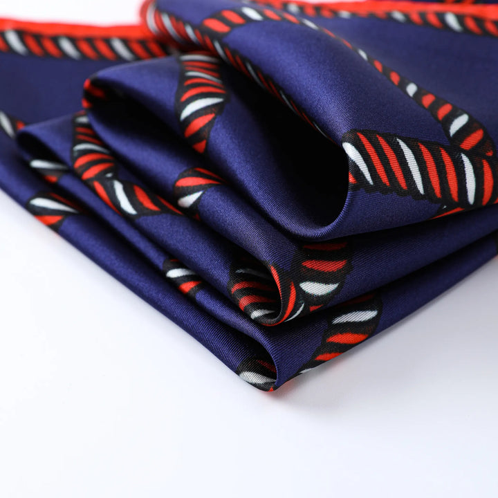 The Witch Hazel Orange Square Silk Scarf from SusanSilk features folded silk fabric in a blue hue with a red, white, and black intertwined rope pattern on a white background.
