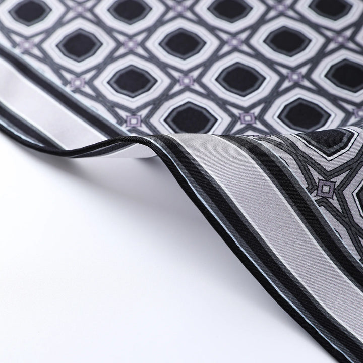 Close-up of the Sakuma Gray Square Silk Scarf by SusanSilk, showcasing a geometric diamond pattern in black, white, and light purple. The luxurious fabric is further accentuated by a contrasting striped border.