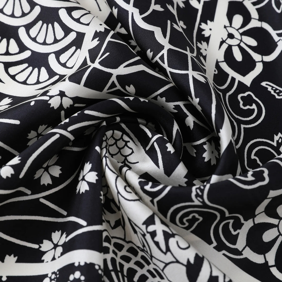 Close-up of the Seeker Black Square Silk Scarf by SusanSilk, showcasing its white floral and abstract design pattern elegantly gathered in the center.