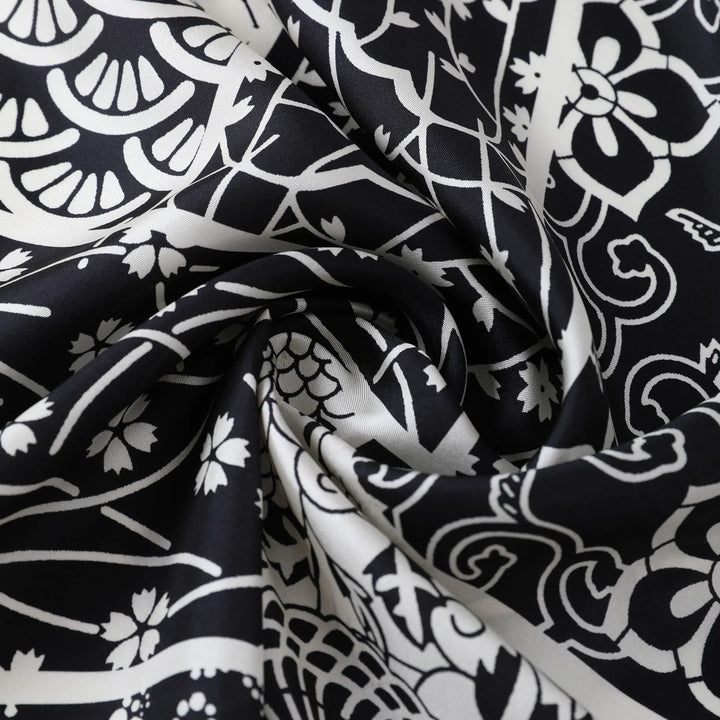 Close-up of the Seeker Black Square Silk Scarf by SusanSilk, showcasing its white floral and abstract design pattern elegantly gathered in the center.