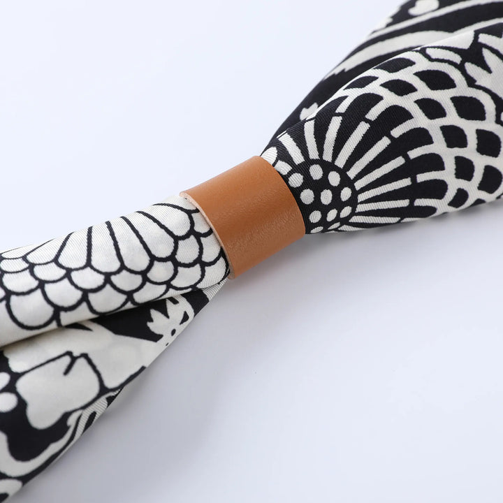 Close-up of the Seeker Black Square Silk Scarf by SusanSilk, featuring a black and white pattern with a tan leather knot in the center.