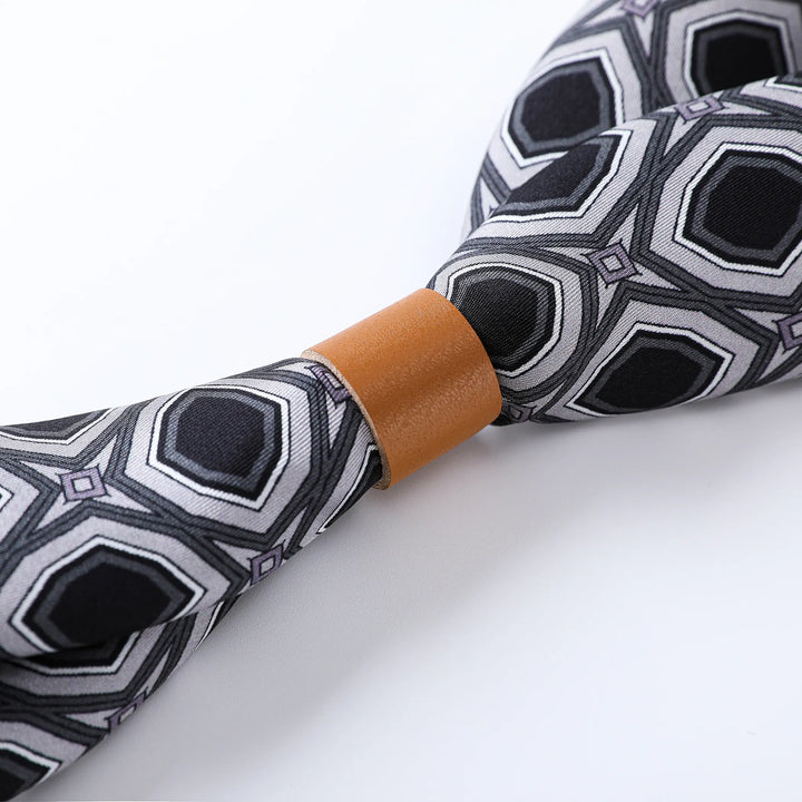 A close-up of a Sakuma Gray Square Scarf showcasing a geometric pattern with black, white, and gray hexagons, crafted from luxurious SusanSilk with a tan leather centerpiece.