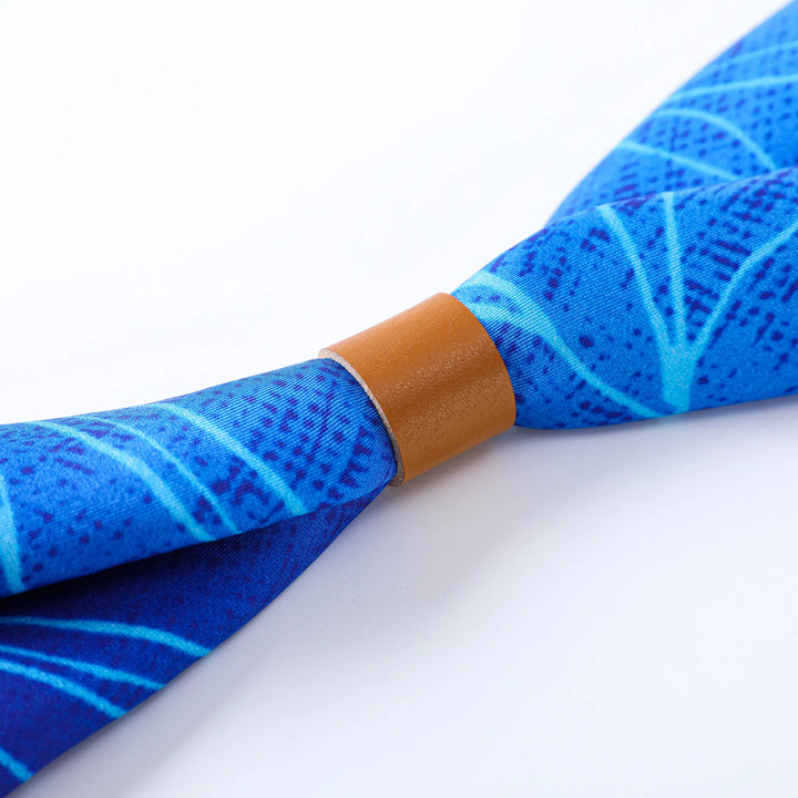 A close-up of the Blue Sky Square Silk Scarf by SusanSilk, featuring intricate light blue leaf patterns and secured with a brown leather band, against a pristine white background.