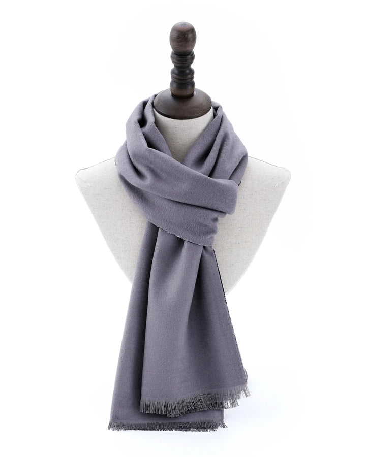 A dusty purple-gray knit scarf with fringed edges, draped on a light gray fabric mannequin bust with a dark wooden neck cap, set against a plain white background.#color_silver