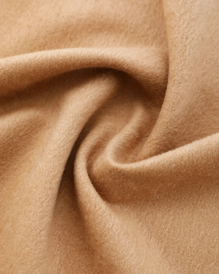 A close-up of soft camel-colored fabric with a smooth, slightly fuzzy texture, arranged in gentle folds and swirls.#color_antique-gold