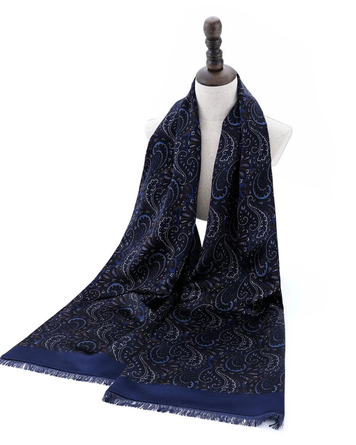 A navy blue scarf with a detailed paisley pattern and fringed edges, draped on a white dress form mannequin against a plain white background.#color_navy-blue