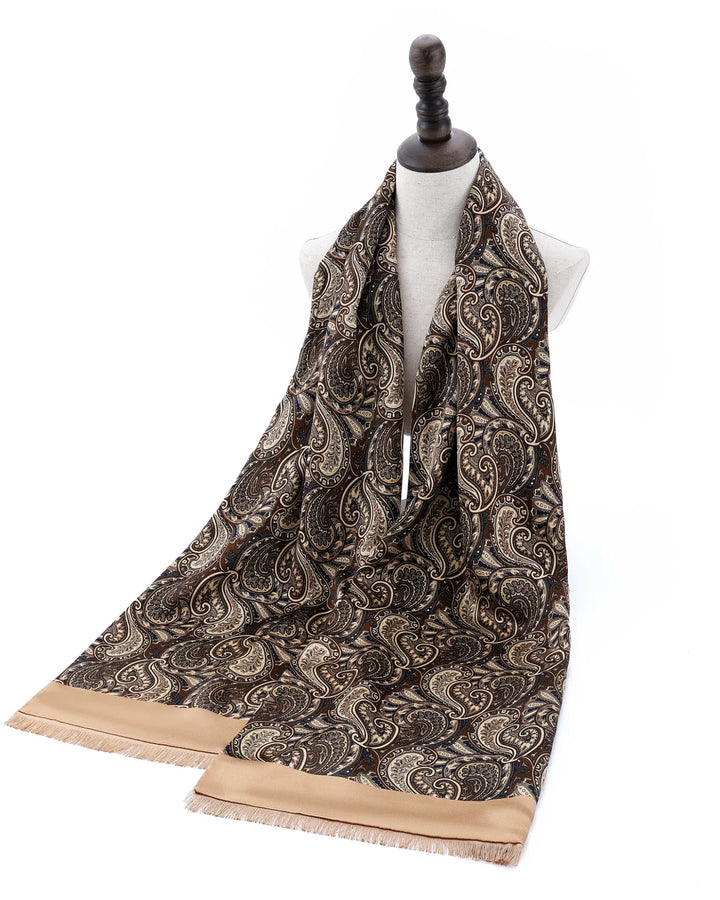 A long paisley scarf draped on a white dress form mannequin, featuring a dark brown and beige paisley pattern with solid beige fringed ends, set against a plain white background.#color_antique-gold