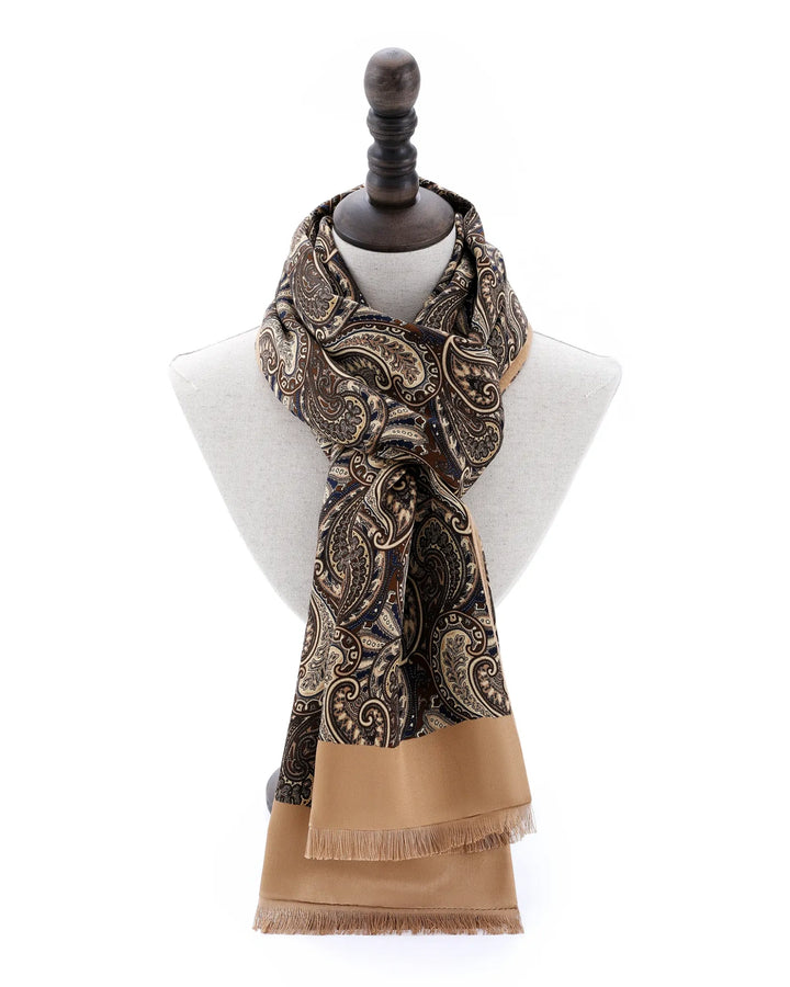 A patterned scarf with a tan border and fringe, displayed on a white mannequin bust against a white background.#color_antique-gold