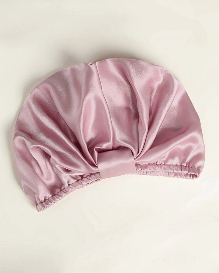Blush pink mulberry silk sleep bonnet laid flat, elegant wrapped front and pleated design, pure silk hair bonnet