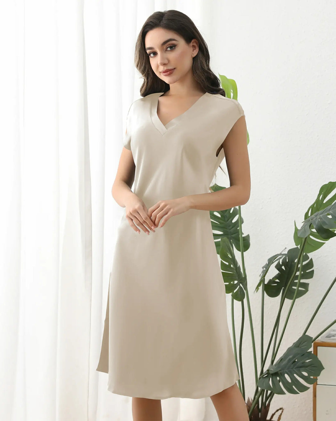 A woman in a knee-length 22 Momme Comfortable Silk Nightdress by SusanSilk holds one hand near her face, smiling with her eyes closed.#color_champagne-gold