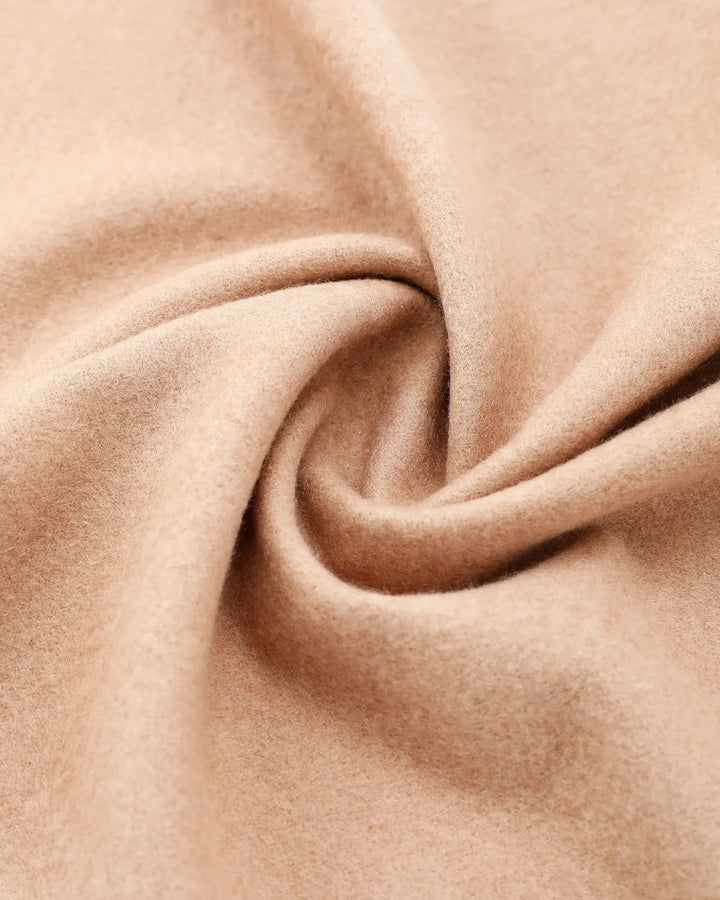 A close-up of soft, draped fabric in a warm light beige or camel color, arranged in a spiral fold to show texture and drape.#color_antique-gold