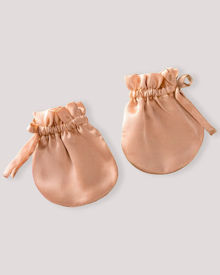 ​​A baby wearing ivory 19 momme silk gloves, gently preventing face scratching while allowing natural hand movement.​​