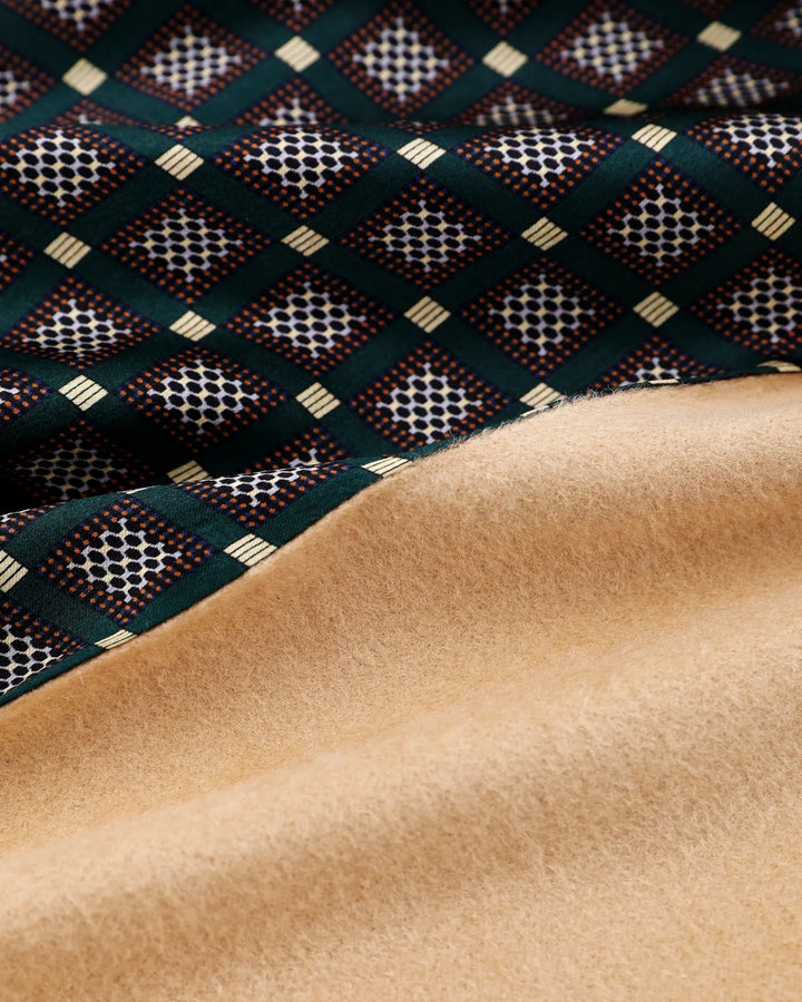 A close-up of a folded textile showing a dark green patterned side with cream and red geometric motifs and a smooth tan suede-like reverse side.#color_forest-green